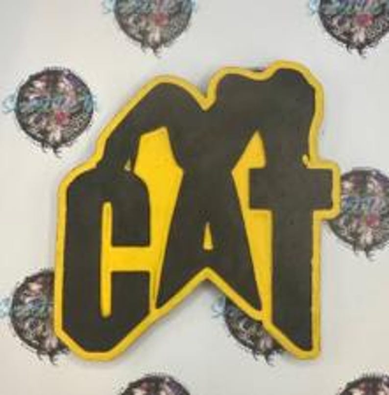 Puede incluir: Un logotipo CAT amarillo y negro, con la palabra "CAT" en una fuente audaz y estilizada. El logotipo tiene un contorno negro y un interior amarillo. El fondo es de color claro con varios dise&ntilde;os circulares.
