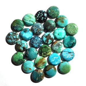 May include: A collection of round turquoise gemstones in various shades of blue and green. The stones have unique patterns and textures, with some displaying brown and black matrix. The gemstones are arranged on a white surface.