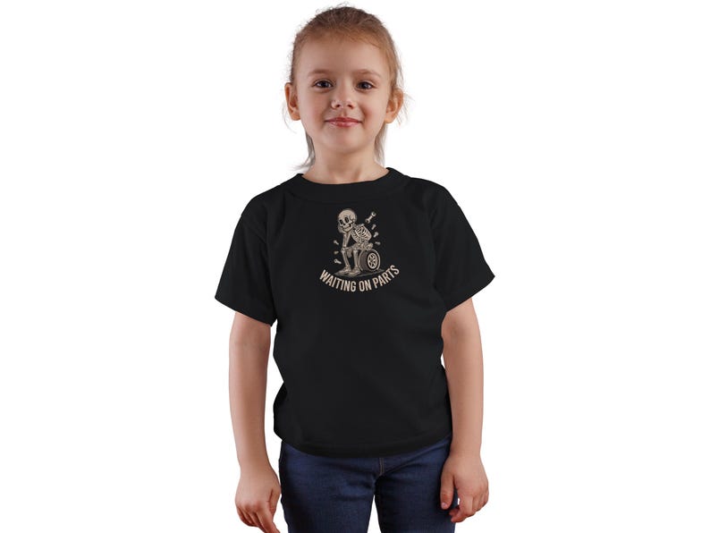 May include: Black t-shirt featuring a skeleton design with the text "WAITING ON PARTS". The graphic shows a skeleton sitting on a tire, with a thoughtful expression. The shirt is worn by a young person.