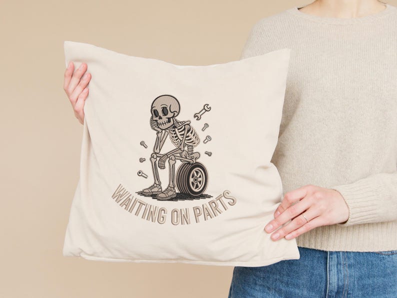 May include: Beige throw pillow with a distressed graphic of a skeleton sitting on a tire, surrounded by wrenches. The text "WAITING ON PARTS" is printed below the skeleton in a matching font.