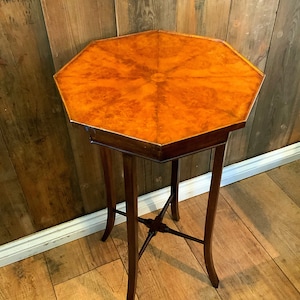 May include: Octagonal wooden table with a brown wood top and a starburst pattern. The table has four legs and a cross-shaped base.