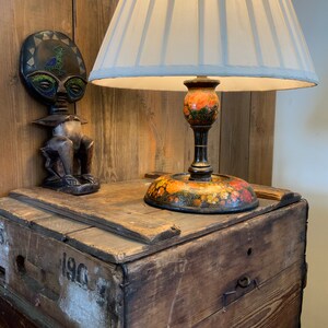 May include: A wooden box with the number 190 on the side, a lamp with a white lampshade and a floral base, and a wooden figurine with a circular head.