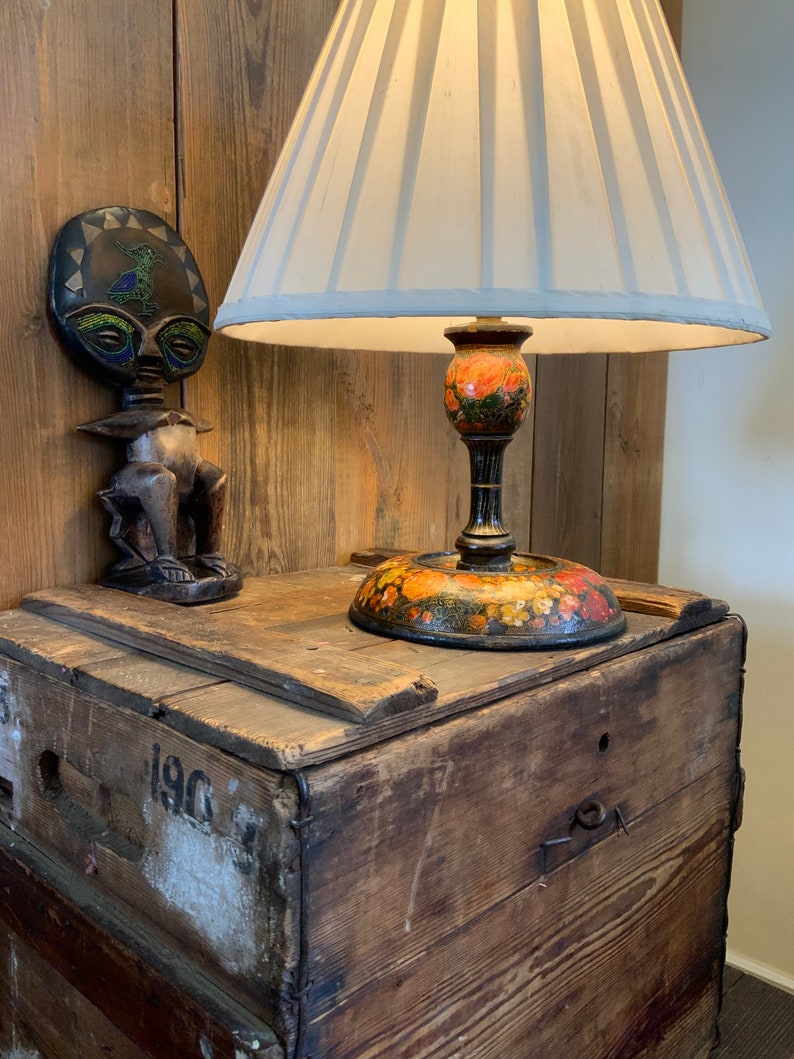 May include: A wooden box with the number 190 on the side, a lamp with a white lampshade and a floral base, and a wooden figurine with a circular head.