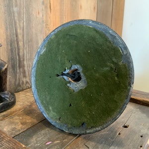 May include: The bottom of a round, dark gray lamp base with a green felt covering. The felt is worn and has a hole in the center.
