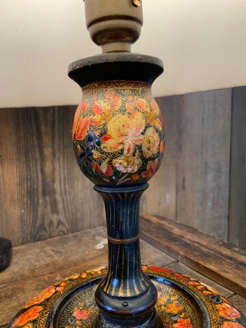 May include: A black wooden lamp base with a floral design painted in shades of orange, yellow, and green. The base has a round, decorative tray at the bottom.