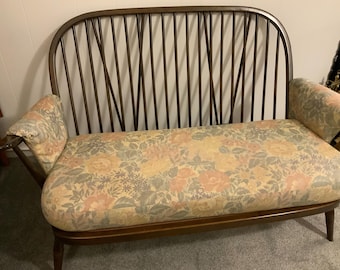 Könnte beinhalten: Eine antike Holzcouch mit geschwungener Rückenlehne und Armlehnen. Der Rücken hat vertikale Sprossen. Sitzfläche und Armlehnen sind mit einem Blumenmuster in Pfirsich-, Gelb- und Grüntönen gepolstert. Die Couch ist etwa 127 cm lang.