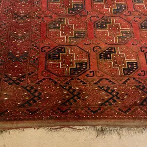 K&ouml;nnte beinhalten: Ein roter, schwarzer und wei&szlig;er Teppich mit Fransen. Der Teppich hat ein geometrisches Muster mit komplizierten Details.