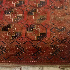 K&ouml;nnte beinhalten: Ein roter, schwarzer und goldfarbener Teppich mit geometrischem Muster. Der Teppich hat einen Fransenrand.