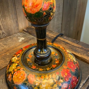 May include: A black wooden lamp base with a floral design painted in shades of orange, red, yellow, and green. The base is round and has a raised rim.