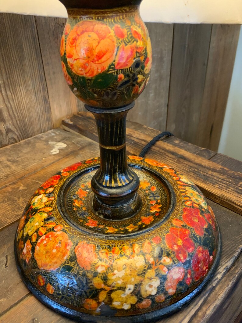 May include: A black wooden lamp base with a floral design painted in shades of orange, red, yellow, and green. The base is round and has a raised rim.