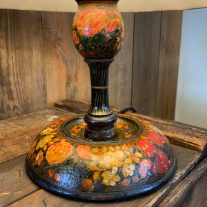 May include: A black wooden table lamp with a floral design. The lamp base is painted with orange, red, and yellow flowers on a black background. The lampshade is not visible in the image.