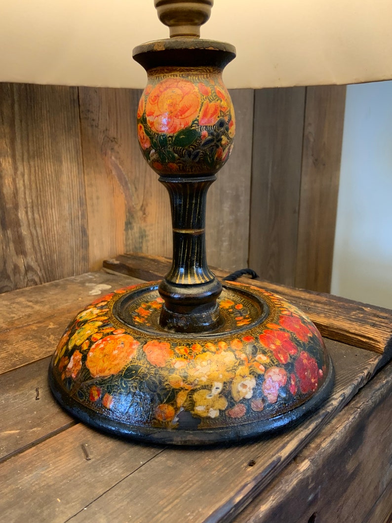 May include: A black wooden table lamp with a floral design. The lamp base is painted with orange, red, and yellow flowers on a black background. The lampshade is not visible in the image.