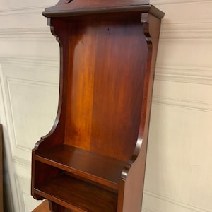 Könnte beinhalten: Ein dunkles Holz-Wandregal mit einem dekorativen Oberteil und einem einzigen Regal. Das Regal ist an einer Wand montiert.