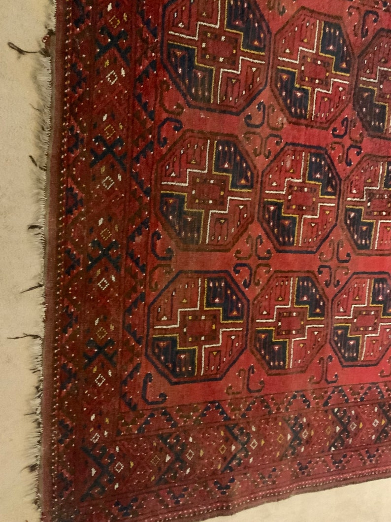 K&ouml;nnte beinhalten: Ein roter, blauer und goldfarbener Teppich mit geometrischem Muster. Der Teppich hat einen Fransenrand und ist aus Wolle.