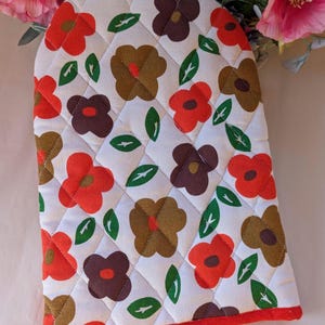 May include: Quilted oven glove with a floral pattern in red, brown, and green on a white background. The glove has a red trim and a diamond-stitched design. A kitchen accessory.