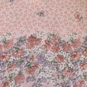 May include: A light pink floral fabric. The fabric has a pattern of small leaves and a border of flowers in shades of pink, white, and purple. The flowers are in full bloom. The fabric is suitable for various craft projects.