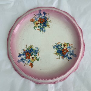 May include: A white ceramic plate with a pink rim and three floral designs. The flowers are blue, yellow, orange, and red.