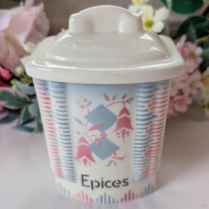 May include: A ceramic spice jar with a lid, featuring a design of blue and pink floral patterns and vertical stripes. The word "Epices" is printed on the front of the jar.