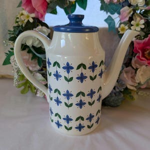 May include: White ceramic coffee pot with a blue lid and a floral pattern of blue flowers and green leaves.