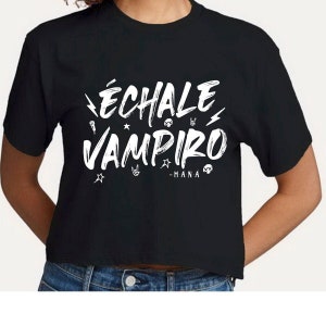 May include: Black crop top with the white text "ÉCHALE VAMPIRO - MANÁ" in a stylized font. The design includes lightning bolts, stars, a microphone, a skull, and a hand gesture. The shirt is made of a soft material.