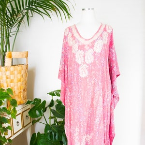 May include: A pink and white patterned kaftan with a V-neck and short sleeves. The kaftan is made of a lightweight fabric and has a flowing silhouette.