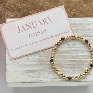 May include: Gold beaded bracelet with four garnet beads. The bracelet is accompanied by a card that reads "JANUARY GARNET vitality ♥ energy ♥ passion ♥ loyalty ♥ protection"