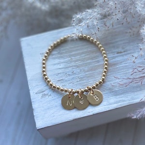 May include: Gold beaded bracelet with three charms: a heart, the letter N, and the letter B.