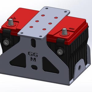 Puede incluir: Una batería automotriz roja y negra asegurada por un soporte metálico gris. El soporte tiene múltiples agujeros y las letras "GGM" son visibles. Los terminales de la batería son plateados.