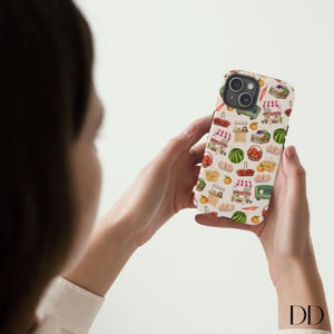 May include: A phone case featuring a repeating pattern of farmers market scenes. The design includes illustrations of market stalls, baskets of produce, watermelons, and oranges on a cream-colored background.