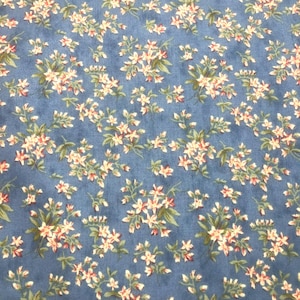 May include: A blue fabric featuring a repeating pattern of small white and cream-colored flowers with green leaves and stems. The floral design is evenly distributed across the surface, showcasing delicate petals and foliage on a solid blue background.