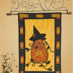 May include: A quilt pattern for a pumpkin-shaped witch with a black hat and a star on its chest. The quilt is 11 1/2 inches by 17 1/2 inches and includes a pattern for a black witches hat. The pattern is called "Promises...Pumpkin" and is by RagSpun.