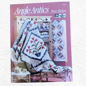 May include: A book titled "Angle Antics" by Mary Hickey, featuring a quilt with a floral design and a white wicker chair. The book is from "The Patchwork Place".