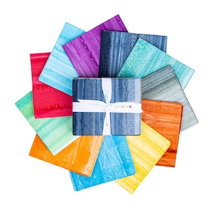 May include: A collection of colorful fabric squares arranged in a circular pattern. The squares display watercolor-like patterns in shades of red, orange, yellow, blue, green, purple, and gray. A bundle of blue fabric squares is tied with a white ribbon.