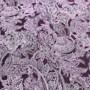 Może przedstawiać: Zbliżenie tkaniny z wzorem paisley w odcieniach fioletu, bieli i czerni. Wzór zawiera skomplikowane motywy kwiatowe i liściaste, tworząc bogatą i szczegółową fakturę. Tkanina ma ciemnofioletowe tło.