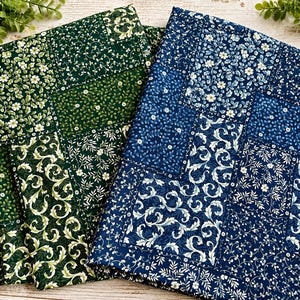 May include: Two folded fabric pieces featuring patchwork designs. One piece displays various shades of green with white floral and vine patterns. The second piece features shades of blue with similar white floral and scrolling vine motifs.