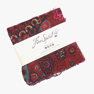 May include: A stack of fabric squares with a floral pattern in shades of red, blue, and yellow. The fabric is wrapped with a white label that reads "FreeSpirit" in cursive. The label also includes social media icons and website information.