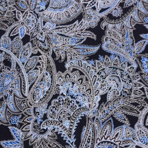 Może przedstawiać: Zbliżenie tkaniny z wzorem paisley. Wzór przedstawia skomplikowane, wirujące kształty w odcieniach niebieskiego, srebrnego i białego na ciemnoniebieskim tle. Wzór jest szczegółowy i ozdobny, tworząc bogaty, teksturowany wygląd.