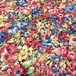 May include: A vibrant floral fabric featuring a dense pattern of colorful blooms. The design showcases red, pink, blue, and yellow flowers with green foliage against a black background. The fabric has a bright and cheerful appearance.