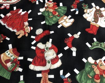 May include: Black fabric featuring a repeating pattern of Christmas-themed paper dolls. The dolls are dressed in red, green, and white outfits, some holding teddy bears. White cut lines surround each doll, creating a playful, vintage aesthetic.