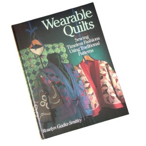 May include: A book titled "Wearable Quilts" with the subtitle "Sewing Timeless Fashions Using Traditional Patterns." The cover features images of quilted jackets in various colors and patterns, including green, blue, and red. The author's name is Roselyn Gadia-Smitley.