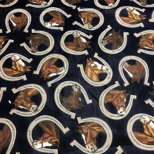 May include: Dark blue fabric with a repeating pattern of brown horses inside silver horseshoes. The horses have tan and white markings and are wearing bridles. The fabric is likely used for quilting or crafting.
