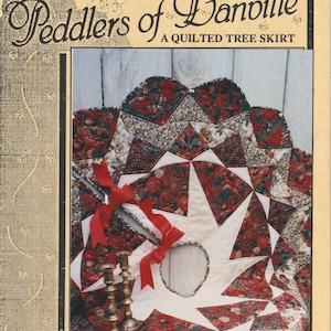 May include: A quilted tree skirt with a starburst design in red, white, and green fabrics. The skirt is decorated with red ribbon bows and gold candle holders. The text "Peddlers of Danville" and "A Quilted Tree Skirt" is printed on the image.
