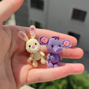 May include: A yellow crocheted bunny and a purple crocheted elephant with pink ears. The toys are small and are being held in a person's hand.