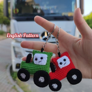 Può includere: Due portachiavi a forma di trattore all'uncinetto, uno verde e uno rosso, con facce sorridenti e ruote nere. I portachiavi sono attaccati a una catena e un anello argentati.