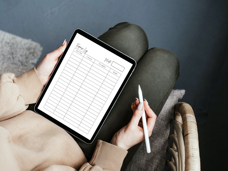Op de afbeelding: Een witte tablet met een lege spreadsheet voor een uitgavenlogboek op het scherm. De tablet wordt vastgehouden door een persoon met een witte stylus in hun hand.