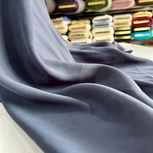 Puede incluir: Primer plano de una tela azul oscuro con una textura suave y sedosa. La tela está drapeada y doblada, mostrando su naturaleza fluida.