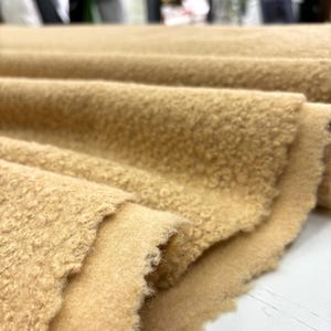 May include: Close-up of a soft, beige fabric with a textured, fuzzy surface. The fabric is folded in layers, showing the texture and colour.