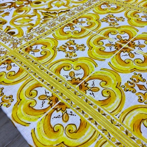 Puede incluir: Mantel blanco con un patrón repetitivo amarillo y marrón de diseños florales estilizados. El patrón se asemeja a un suelo de baldosas.
