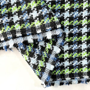 May include: Close-up of a black, blue, and green tweed fabric with a checkered pattern. The fabric has a frayed edge.