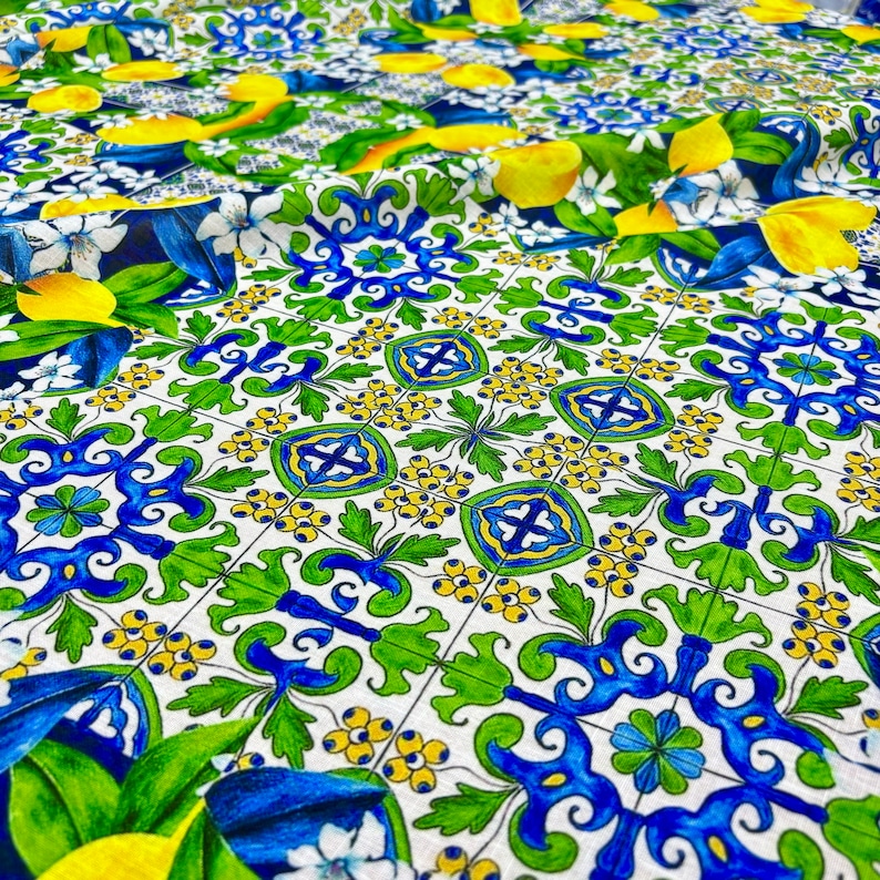 May include: A white fabric with a repeating pattern of blue and green tiles. The tiles have a floral design and are surrounded by yellow lemons and green leaves.